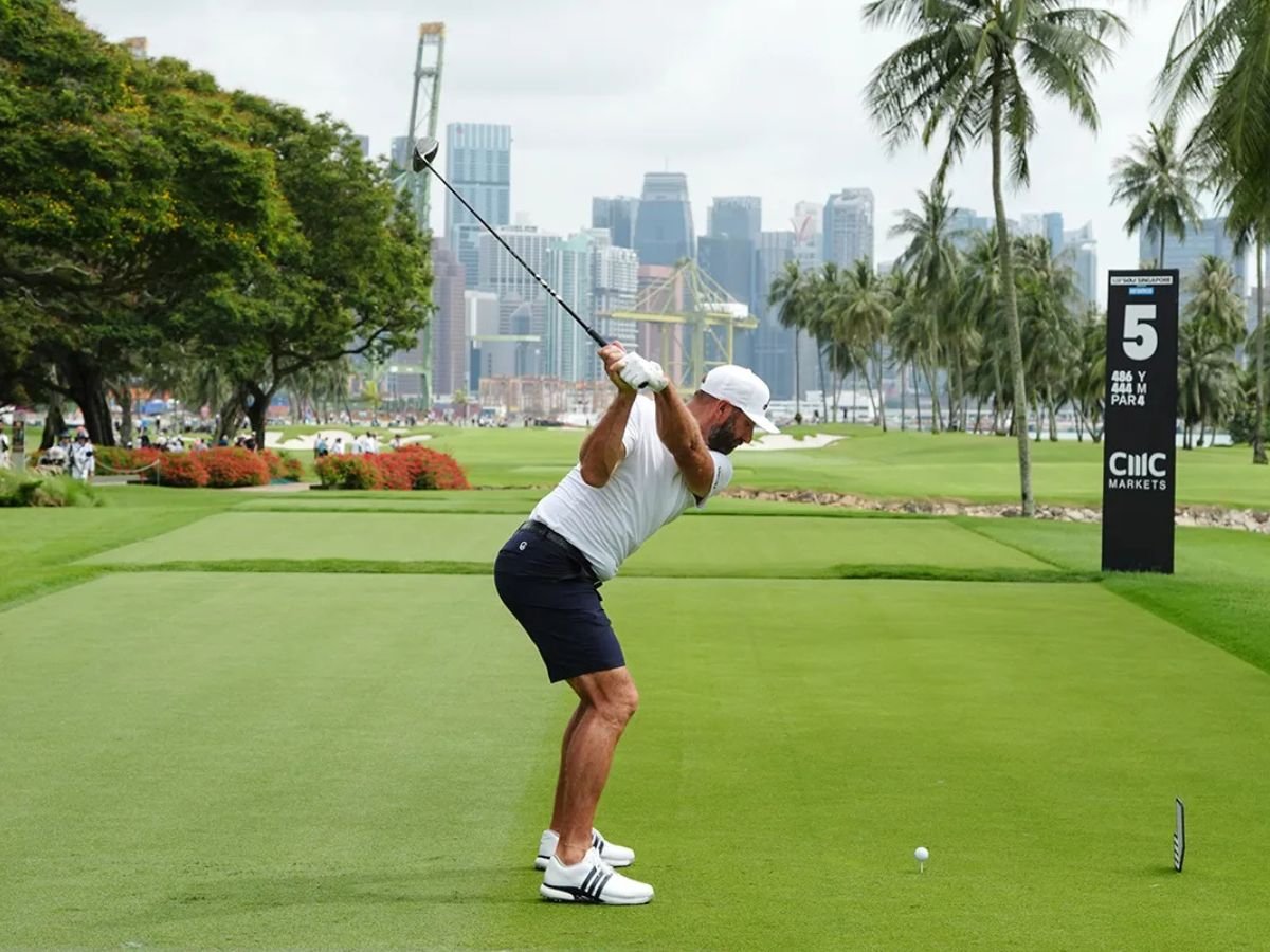 Dustin Johnson takes a tee shot at Sentosa Golf Club during LIV Golf Singapore, with palm trees and Singapore’s skyline in the background.