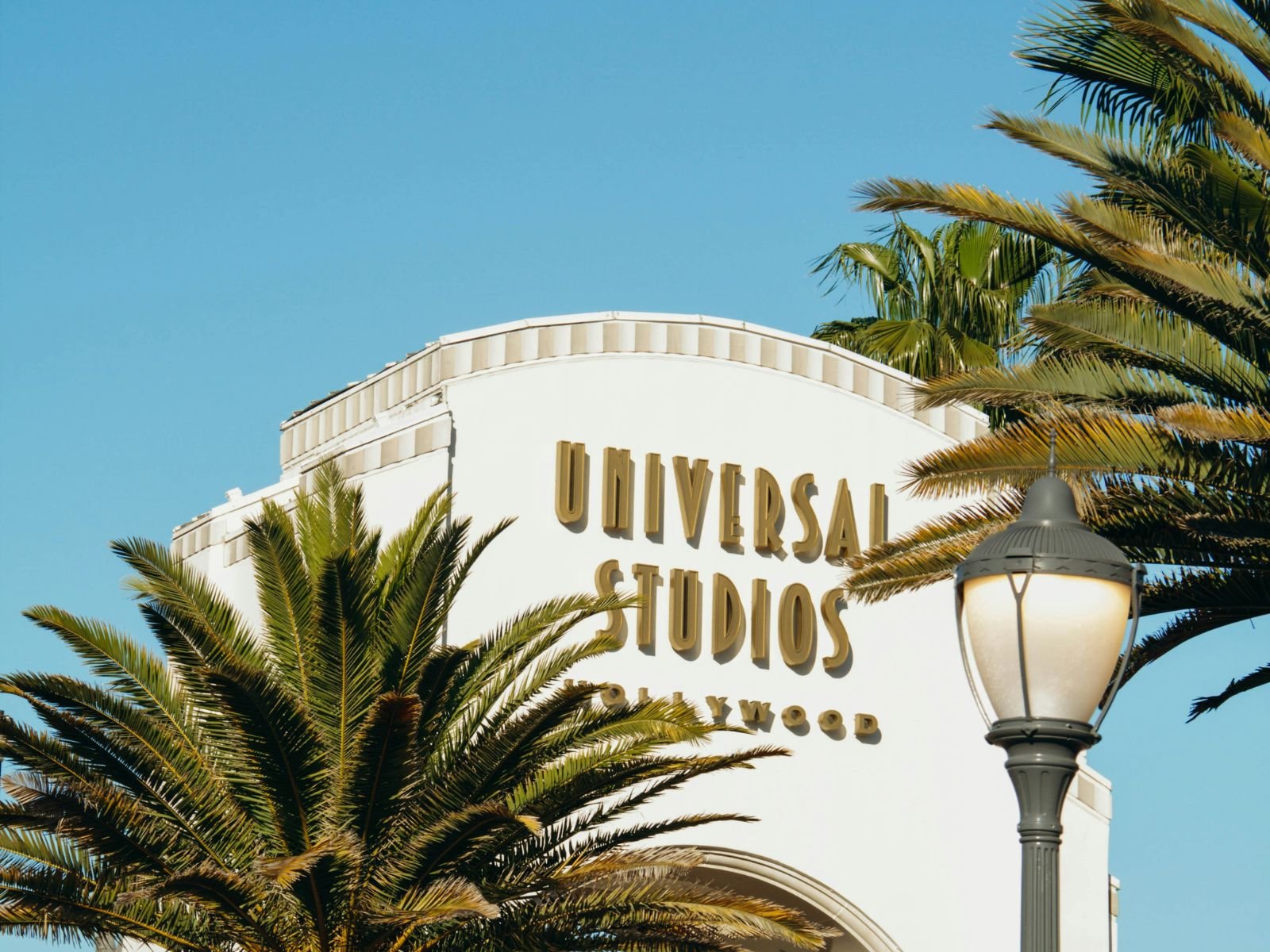 Universal Studios Hollywood entrance arch framed by palm trees beneath a clear blue sky.